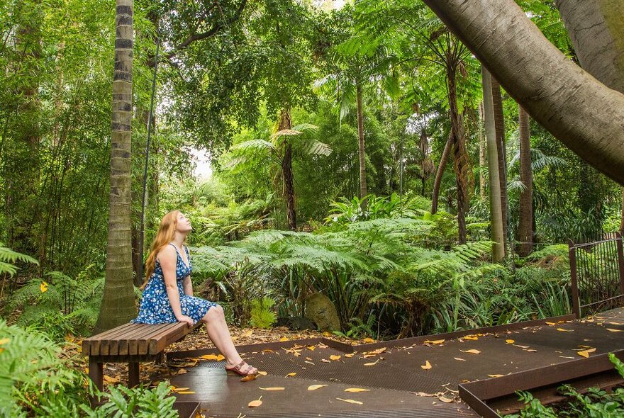 Woman in blue dress sitting in a garden, with face upturned.