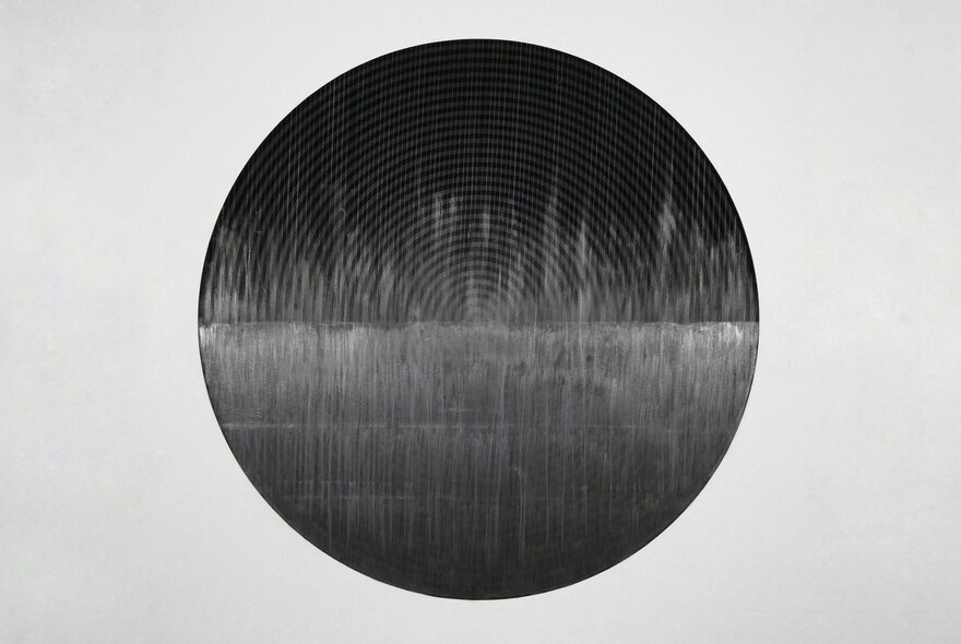A print showing a central black circle with grooves and a horizon line, against a grey background. 