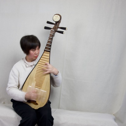 A seated person playing a traditional Chinese pipa, a four-stringed plucked instrument with a pear-shaped wooden body, against a white background.