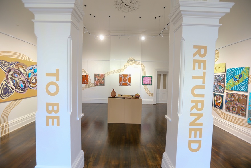 An arched gallery space with polished hardwood floors and First Nations artworks displayed on the walls.