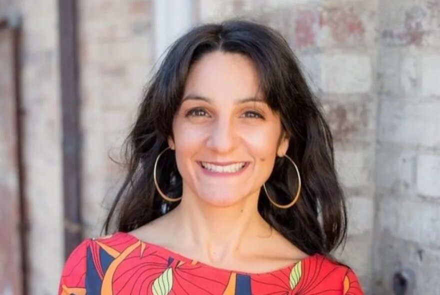 Presenter Paola Di Trocchio, with long dark hair, large hoop earrings and cerise patterned top.
