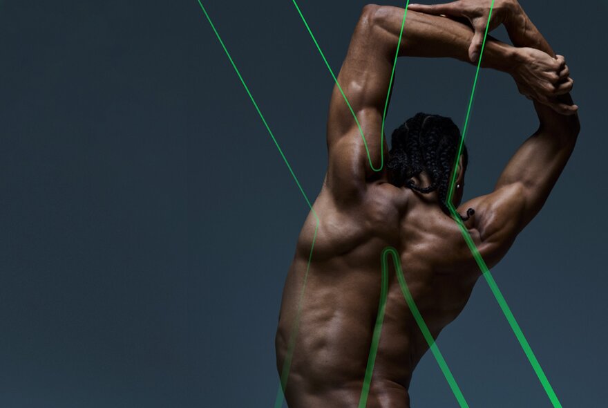 The muscled naked back of a male ballet dancer with his arms crossed above his head; a green neon 'X' outlined over his body.