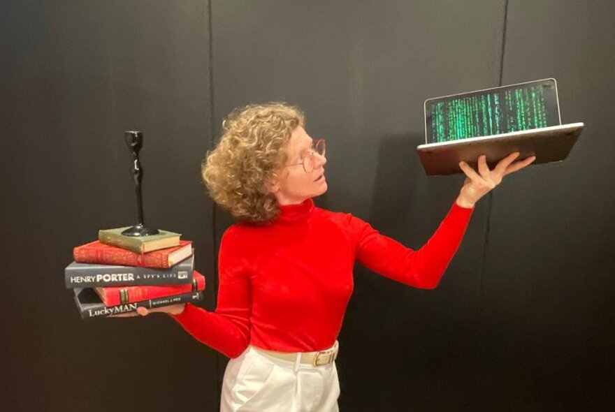 Woman holding a pile of books in one hand, a laptop in the other.