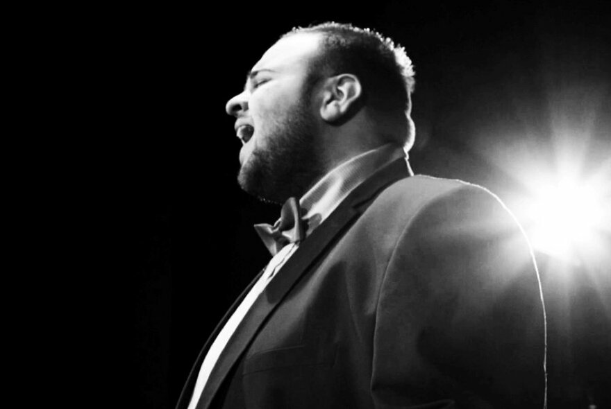 Singer Anthony Gerace performing on stage in front of a spotlight.