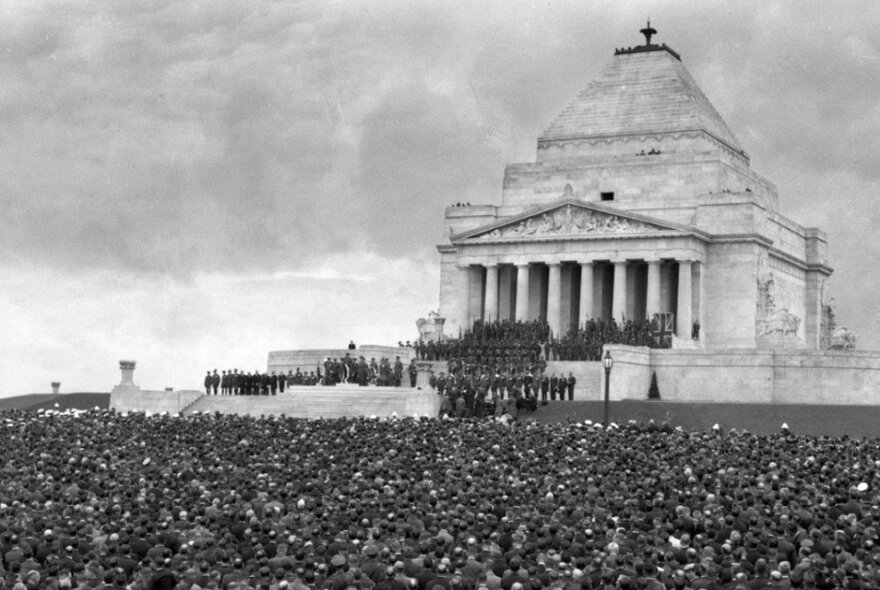 Black and white photo of the Shrine of Remembrance with a large crowd of people in front of it and on the front steps.