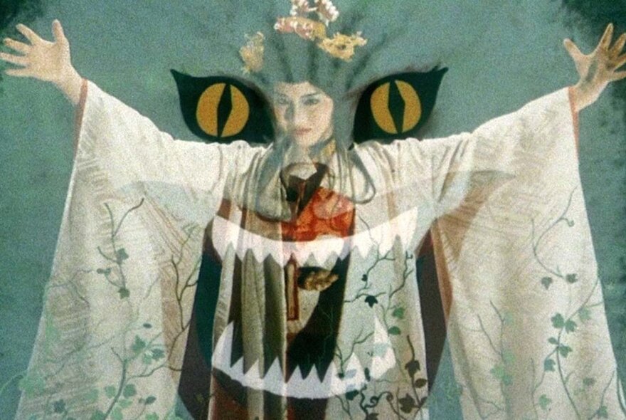 A still from a J-Horror movie, where a Japanese woman in kimono stands with arms spread, with a translucent overlay of a cat's jaws.