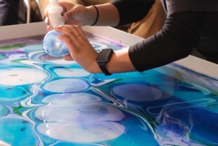 A person performing water marbling with visible paint swirls in blue. 