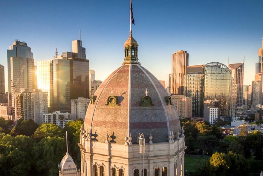 Exhibition Building dome in sunlight, cityscape at rear.