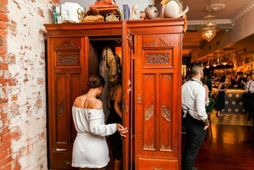 Women walking through a secret passageway inside a wardrobe in a bar. 