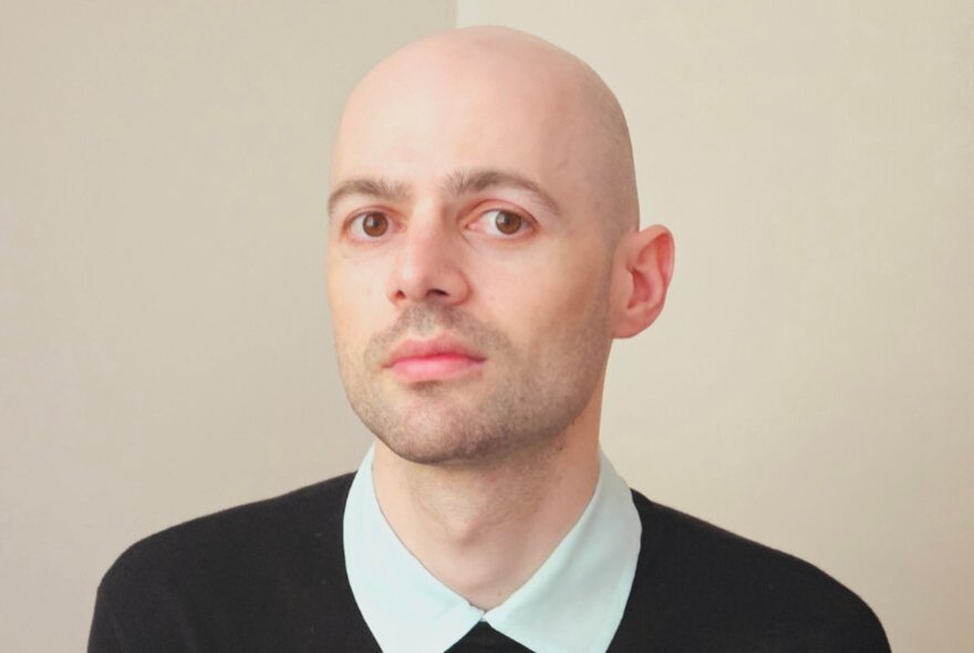 A bald man in a buttoned up shirt looks mildly uncomfortable. 