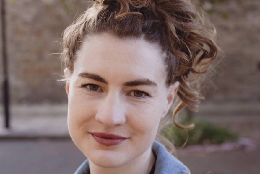 Author Lucia Osborne-Crowley with hair in a ponytail, wearing a denim jacket.