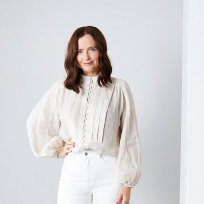 Woman wearing a white blouse and trousers, her hand on her hip.