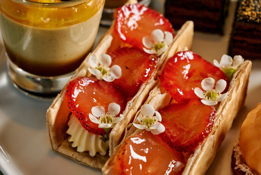 Sweet pastry shells filled with cream, and fresh glazed strawberry slices, served as part of a high tea.