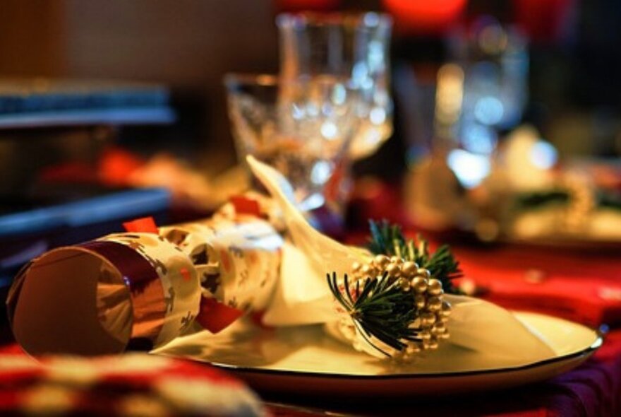 A festive table place setting with a decorative golden pine cone and Christmas bon bon cracker on a plate.