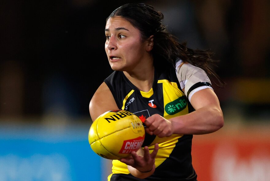 A Richmond AFLW player handballing a yellow Sherrin football.