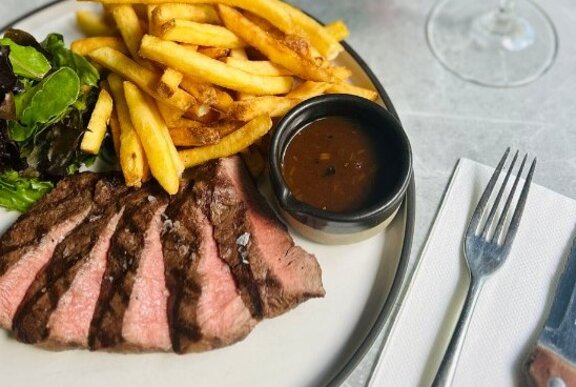 A rare steak, sliced and spread delicately on a plate alongside a handful of fries, a green salad and a sauce ramekin.