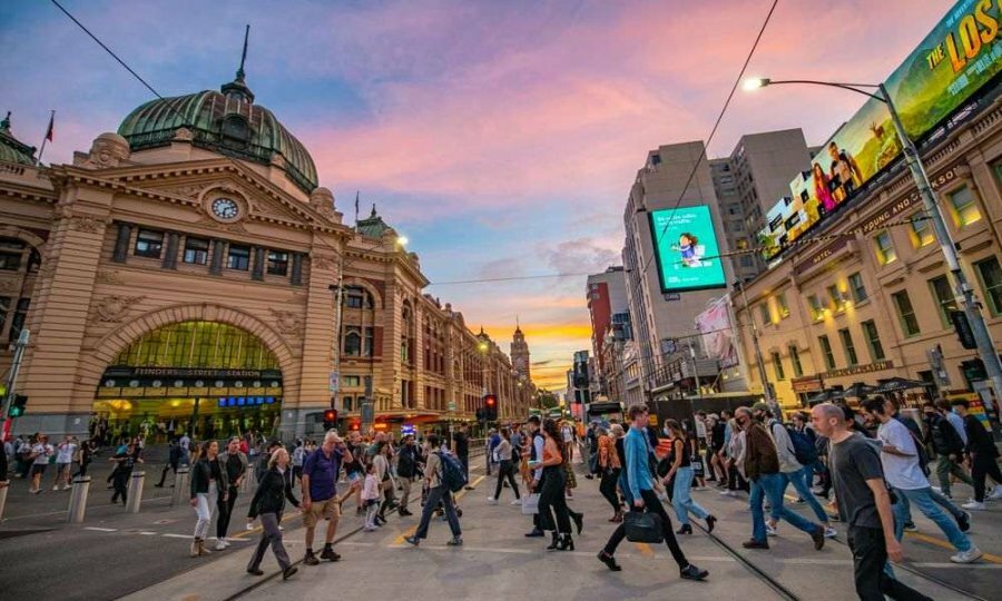 People crossing the road in front of a large train station at sunset