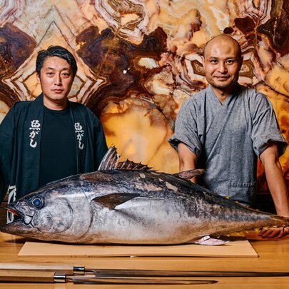 Two Japanese chefs with a large tuna on a chopping board with knives.