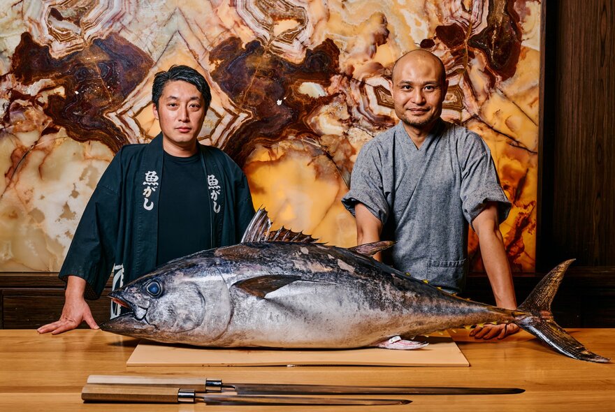 Two Japanese chefs with a large tuna on a chopping board with knives.