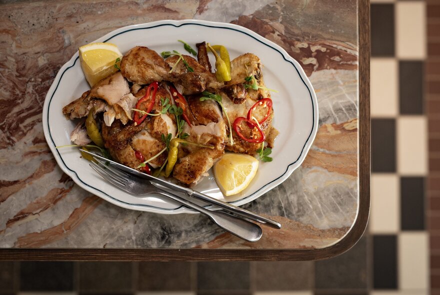 Dish of food with lemon garnish on a plate with cutlery.