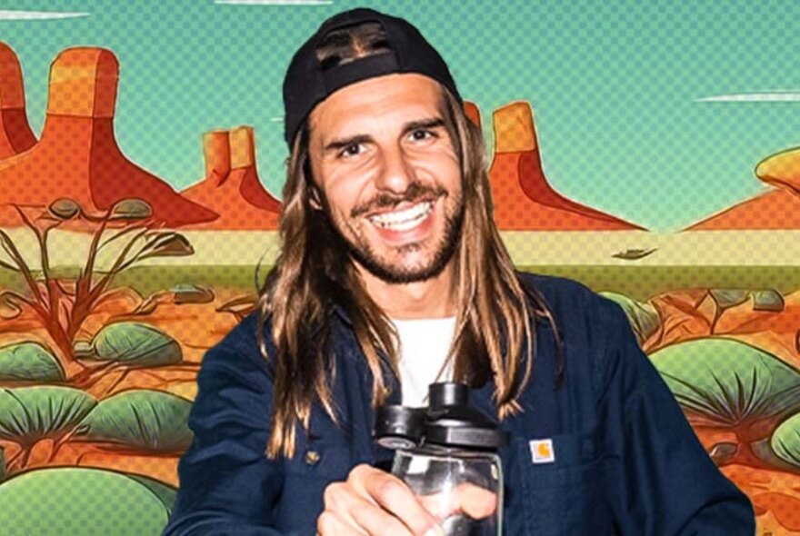 Comedian Craig Conant smiling, his long hair falling either side of his face, wearing a backwards baseball cap, posed in front of a backdrop of a painted desert scene.