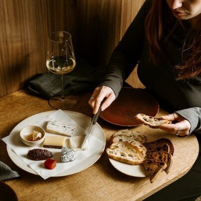 Hands selecting from cheese platter on restaurant table.