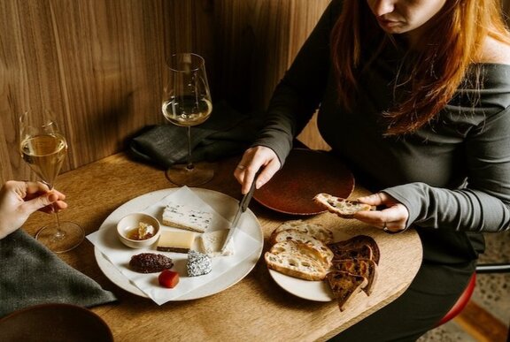 Hands selecting from cheese platter on restaurant table.