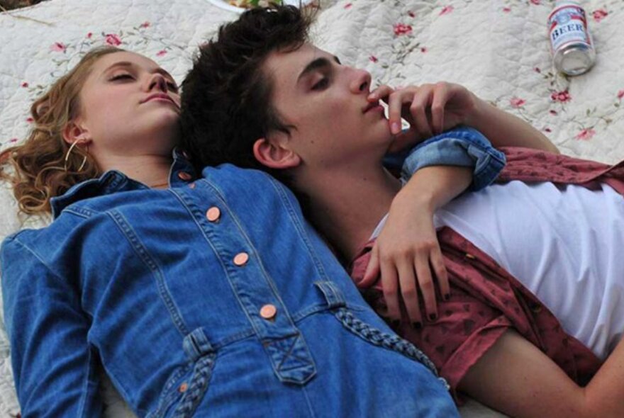 Actor Timothée Chalamet and actor lying on the sand.