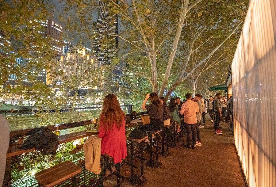 People sitting at an outdoor bar, overlooking the Yarra River. 