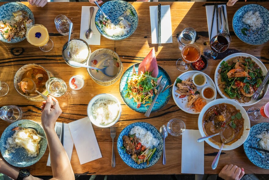 Looking down on a table with many plates of Thai food and several people eating.