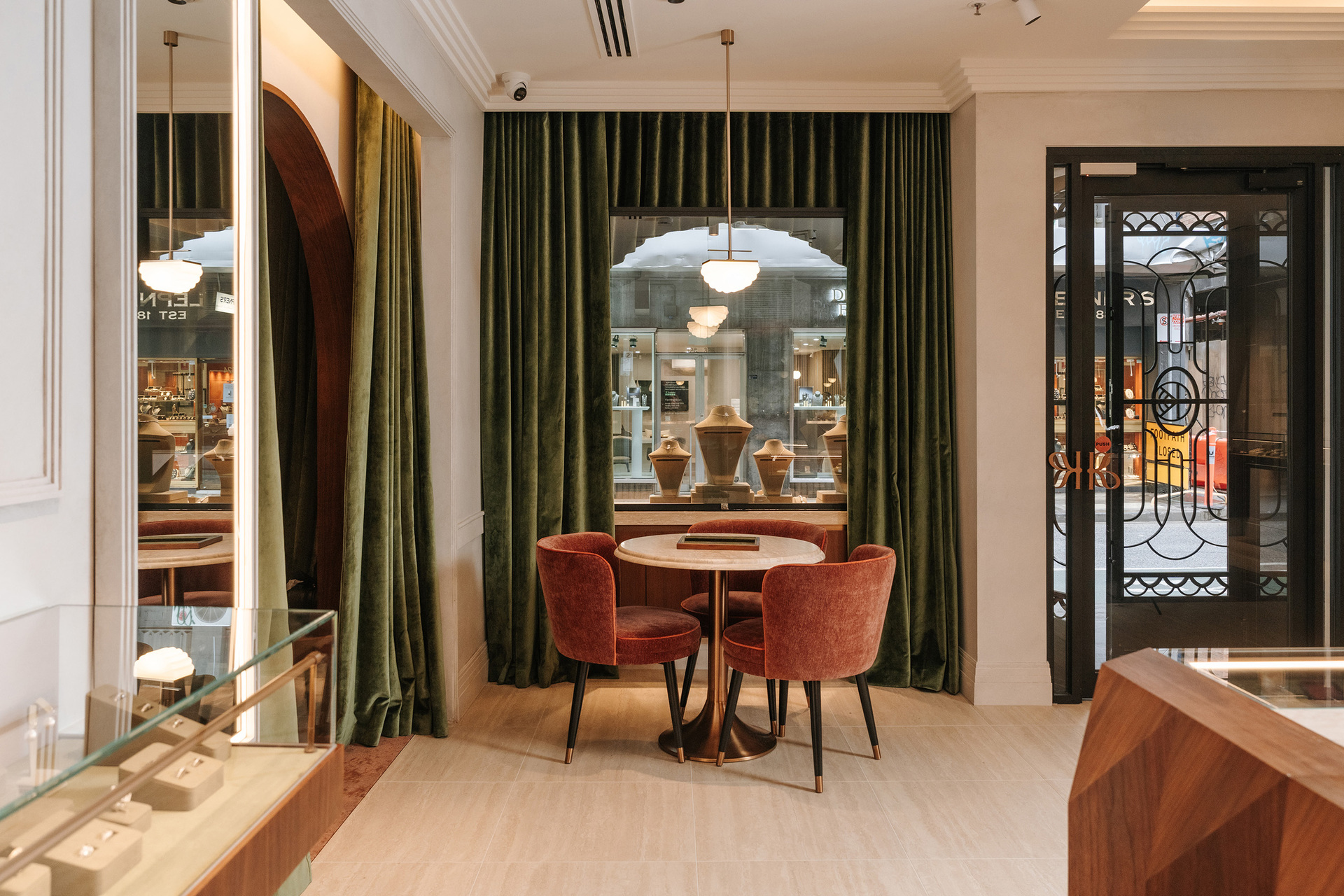 The inside of a jewellery shop with green velvet curtains, a table and chairs and an arched window overlooking the street.