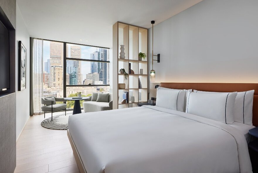 Interior of a luxury hotel room with a king size bed and large window looking out to the Melbourne city skyline.