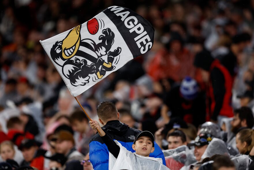 Collingwood AFL football fan waving a large flag with magpie icon from the stands.