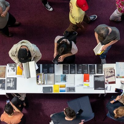 Overhead view of a crowd of people browsing books at book stalls in an interior setting.