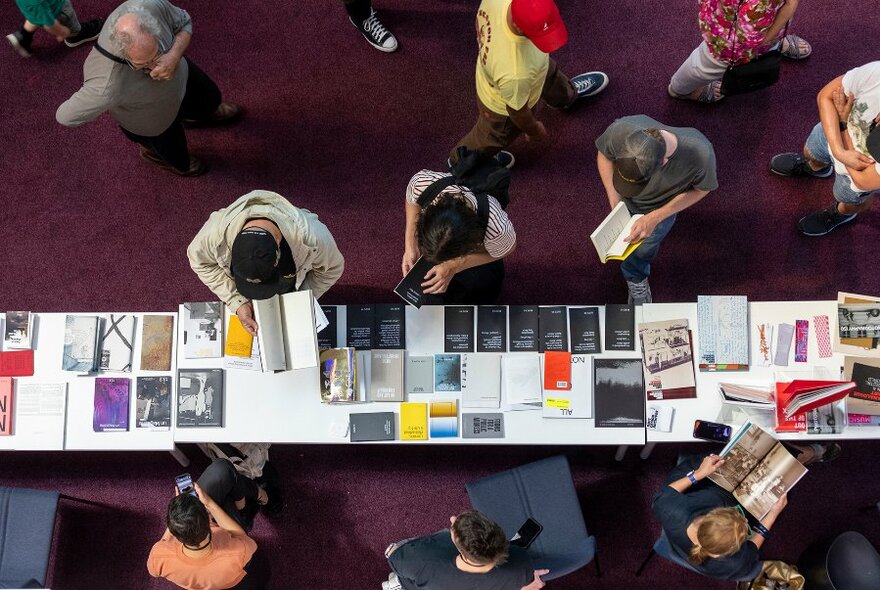 Overhead view of a crowd of people browsing books at book stalls in an interior setting.