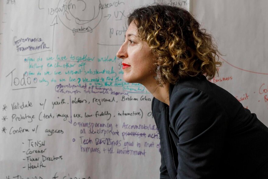 A side view of a woman leaning forward in front of a wall of notes in various shades of ink.