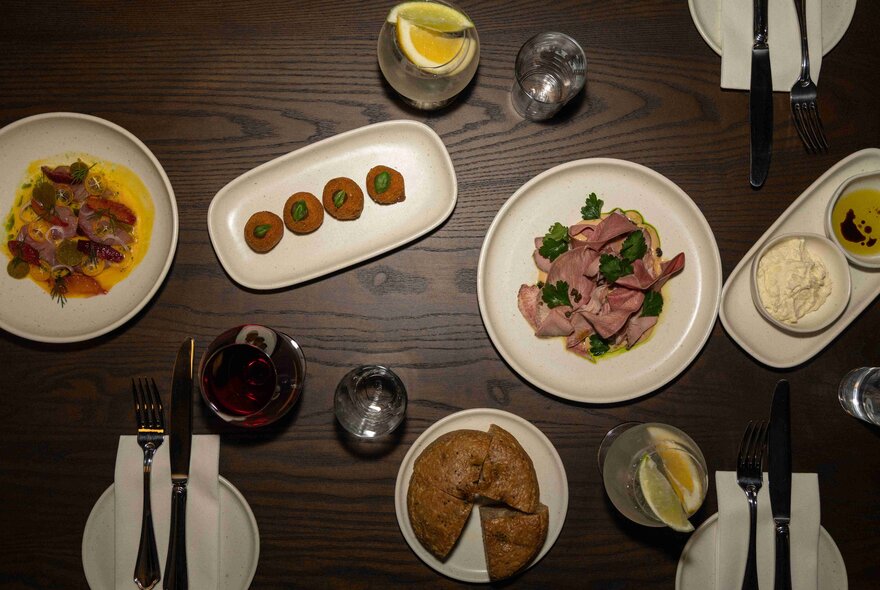Share plates of Italian cuisine seen from above on a wooden table set with small plates and cutlery.