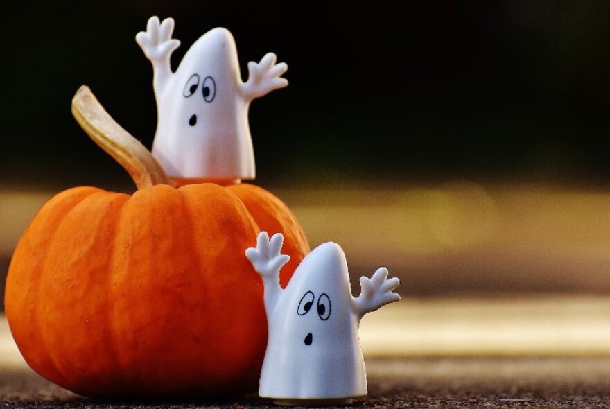 Orange pumpkin with two ghost decorations, with arms raised.