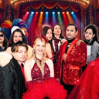 The ensemble cast of a theatre or musical production, dressed in costume, posed in front of a stage.