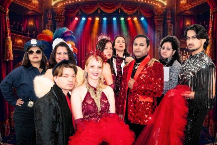 The ensemble cast of a theatre or musical production, dressed in costume, posed in front of a stage.