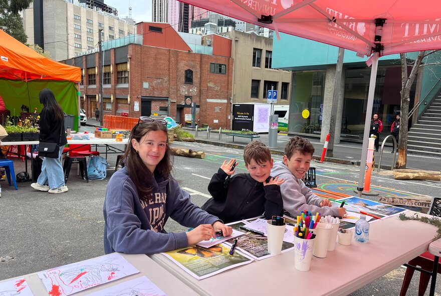 Three children enjoying a drawing workshop at an outdoor event.