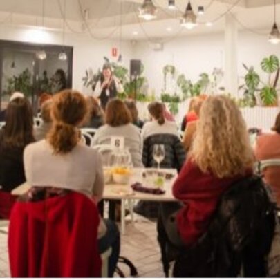 The back view of people sitting in a lit room listening to a speaker. 