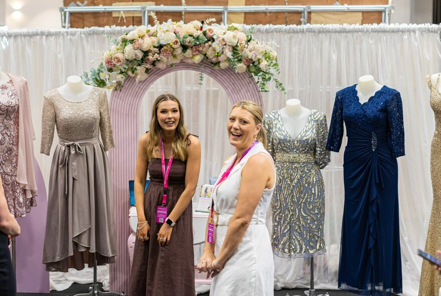 A booth at a wedding expo showcasing dresses with a rose arbor.