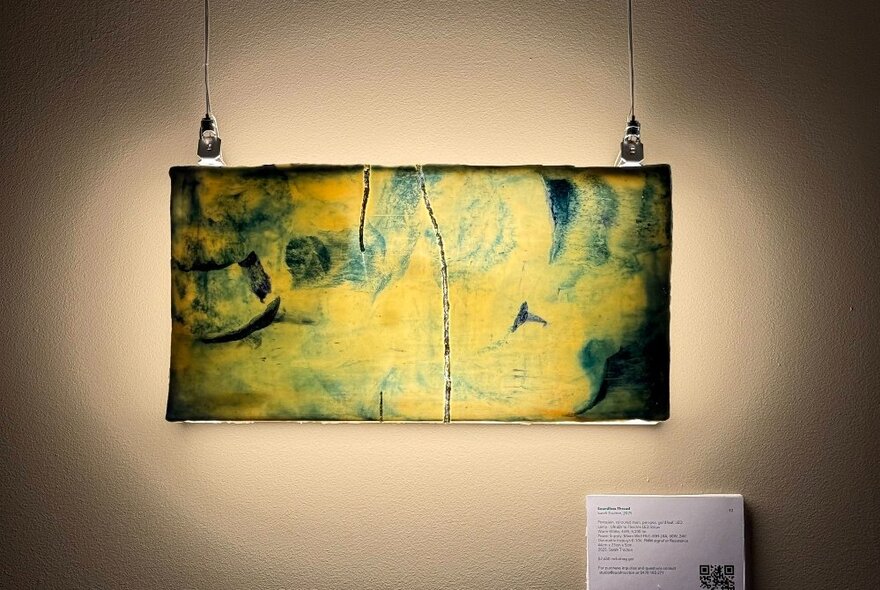 A hanging porcelain artwork on a white wall, with small information panel underneath.