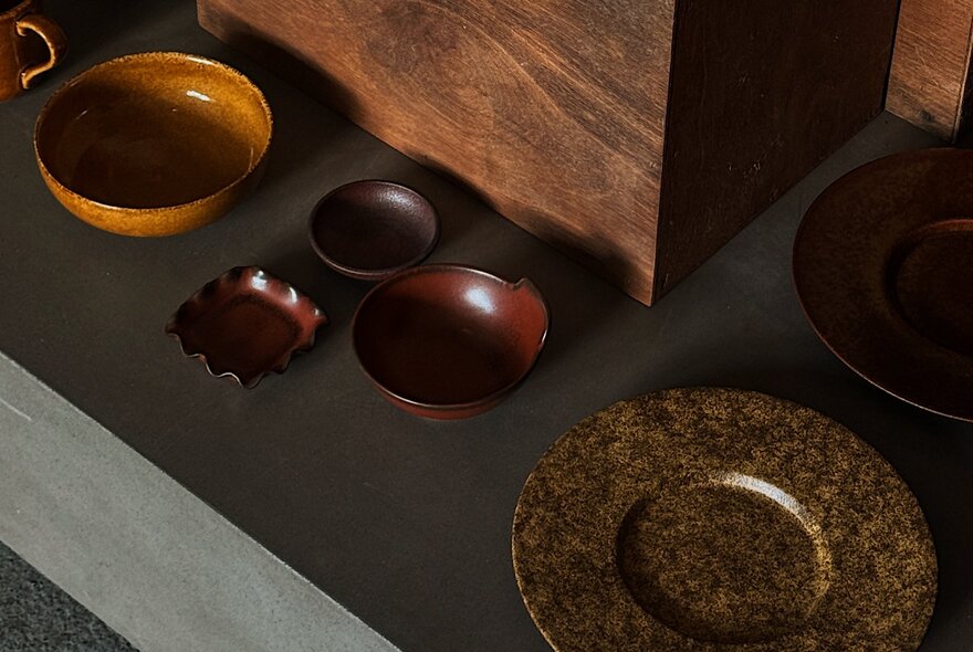 Artisanal wooden and ceramic tableware arranged on a dark surface next to a large wooden block.