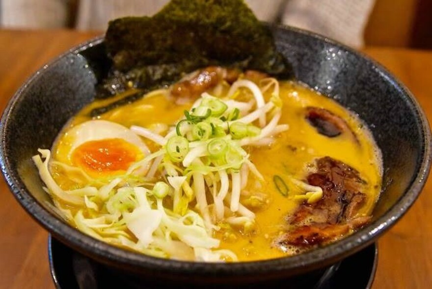 A bowl of ramen with sliced egg, bean sprouts and spring onion.