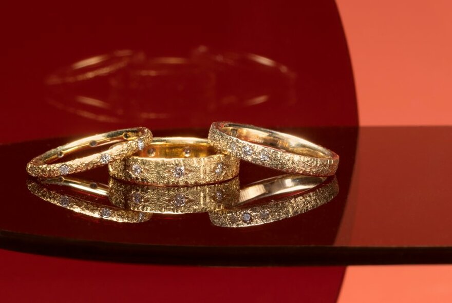 Three gold rings inlaid with jewels on a dark reflective tabletop.