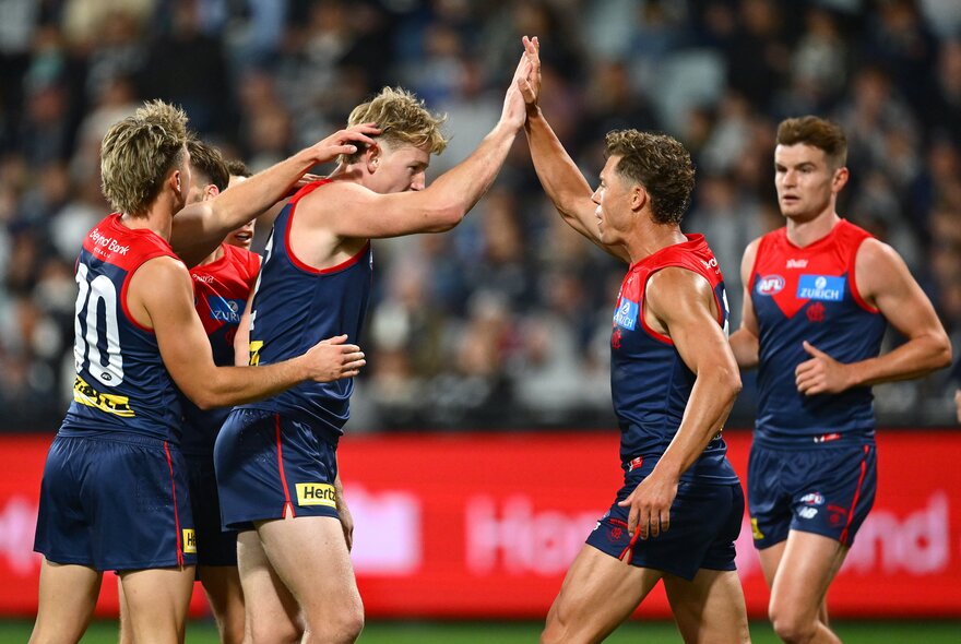 A huddle of Melbourne football players celebrate on the ground. 