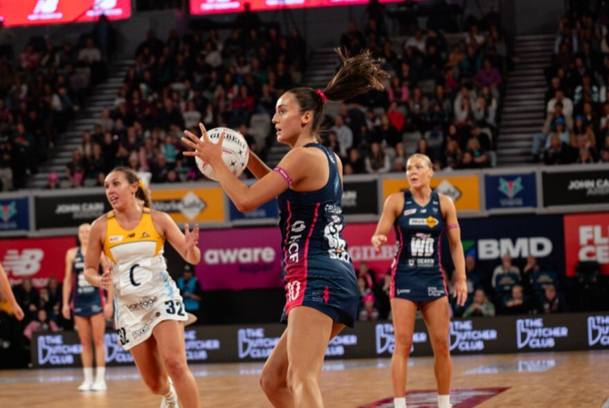 Netball players competing in a game, with one player holding the ball and other players behind her.