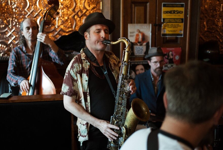 A jazz band playing in a small venue with a saxophonist in a hat up front. 